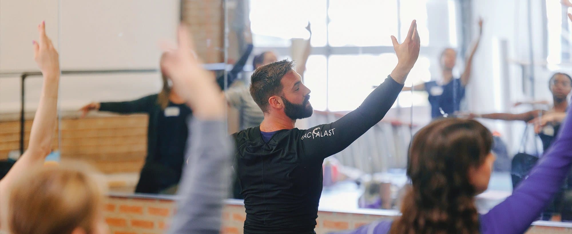 A PBT tutor leading a studio full of dance teachers through a conditioning class, arms raised